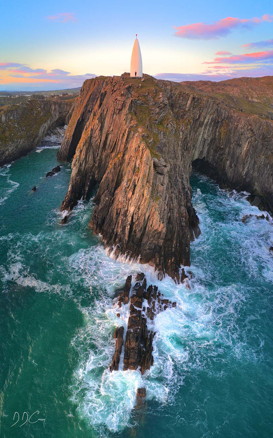 The Beacon at sunset, with waves crashing beneath the cliffs near Baltimore, Ireland. High-resolution photograph captures the rugged beauty of the landmark and surrounding landscape.