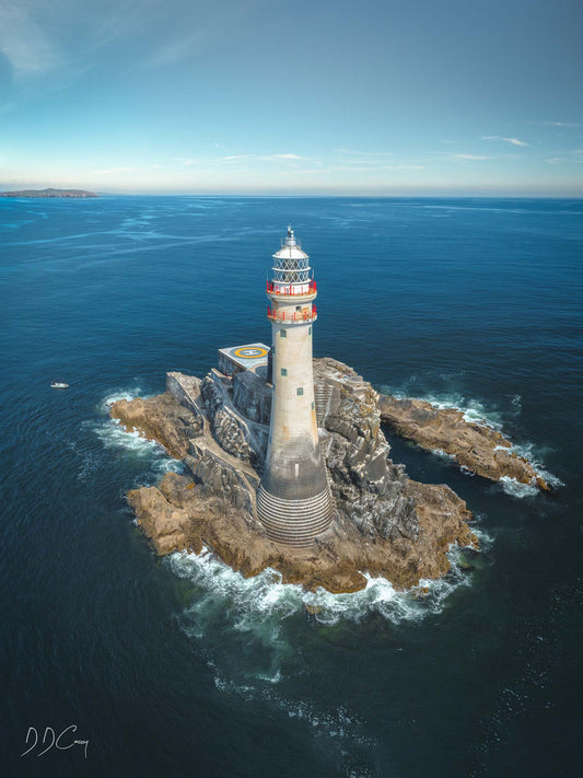 Fastnet Lighthouse standing tall and proud on a calm summer day, with deep blue sea in the background. Built to withstand the harsh Irish weather, this impressive feat of engineering is a symbol of safety and guidance for ships at sea.